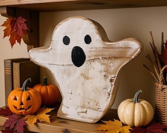 May include: A white wooden ghost cutout with a distressed finish, featuring two black circular eyes and an oval mouth. The ghost is surrounded by orange jack-o'-lanterns, small cream-colored pumpkins, and scattered red and yellow maple leaves.