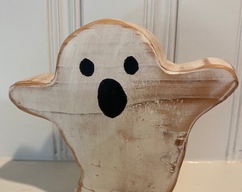 May include: White wooden ghost with black painted eyes and mouth. The ghost is standing on a white surface.
