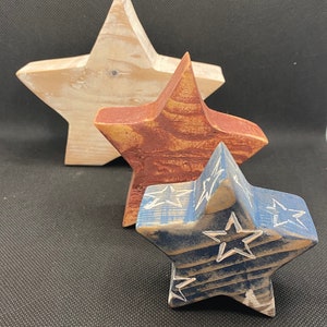 May include: Three wooden stars of different sizes, painted in red, white, and blue. The largest star is white, the middle star is red, and the smallest star is blue with white stars on it.