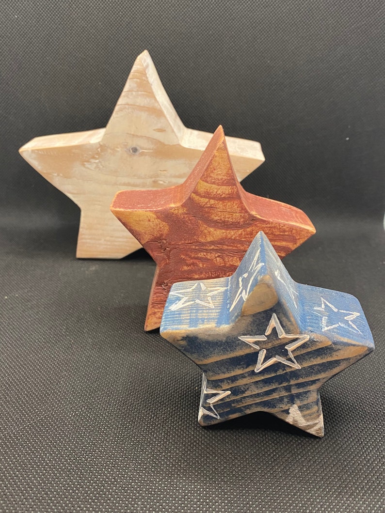 May include: Three wooden stars of different sizes, painted in red, white, and blue. The largest star is white, the middle star is red, and the smallest star is blue with white stars on it.