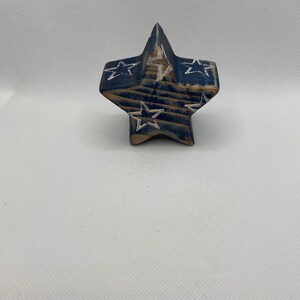 May include: A wooden star-shaped ornament painted in blue and white with a distressed finish. The star has a white star design carved into each point.