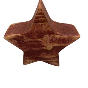 May include: A wooden star ornament painted in a deep red color with a rustic finish. The star is made of wood with visible grain and has a slightly distressed look.