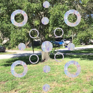 May include: A collection of iridescent, holographic, circular stickers with a variety of designs. The stickers are arranged in a pattern on a green lawn.