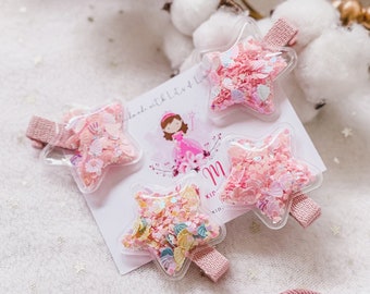 May include: Four pink star-shaped hair accessories with glitter inside. Two are hair clips and two are hair ties.