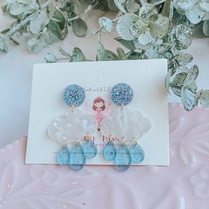 May include: White cloud shaped earrings with blue glitter raindrops hanging from them. The earrings are on a white card with the text "My Little Accessories" and "Etsy.com/shop/for.moonkids" printed on it.