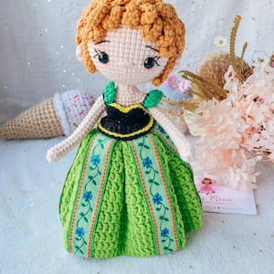 May include: Crocheted doll with brown hair, a green dress with floral embroidery, and a black bodice. The doll has a sweet, cartoon-like face with large eyes.