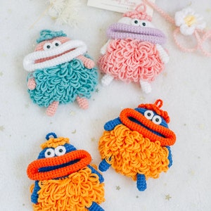Puede incluir: Cuatro juguetes de peluche tejidos a crochet con diferentes colores de pelo y rasgos faciales. Los juguetes tienen ojos grandes, una boca y una m&aacute;scara de crochet blanca. Los juguetes son de varios colores, incluyendo azul, naranja, rosa y verde.