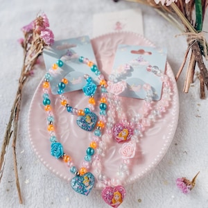 Pode incluir: Dois conjuntos de colares e pulseiras com tema de princesa. Os colares apresentam pingentes em forma de cora&ccedil;&atilde;o com imagens de princesas. As pulseiras s&atilde;o feitas de contas transparentes com detalhes coloridos.