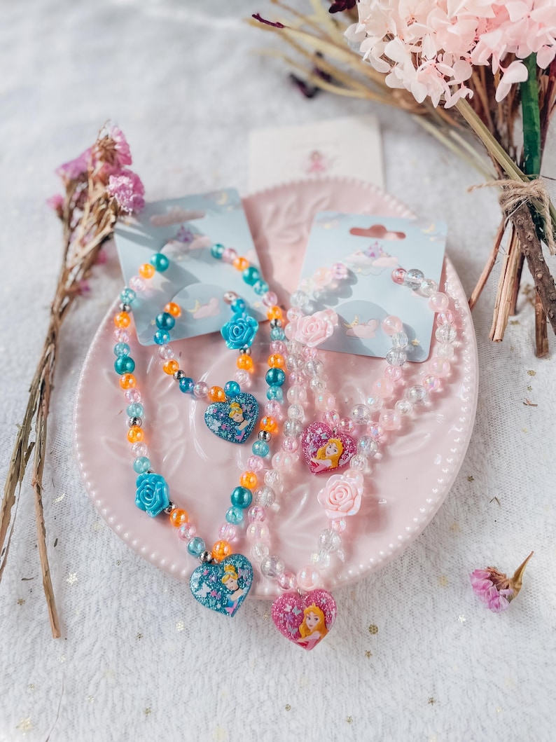 Pode incluir: Dois conjuntos de colares e pulseiras com tema de princesa. Os colares apresentam pingentes em forma de cora&ccedil;&atilde;o com imagens de princesas. As pulseiras s&atilde;o feitas de contas transparentes com detalhes coloridos.