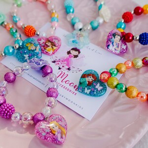 May include: A set of colorful beaded bracelets with heart-shaped charms featuring Disney princesses. The bracelets are made with various colors of beads, including pink, purple, blue, green, red, and yellow. The charms feature princesses like Ariel, Cinderella, Rapunzel, and Snow White.