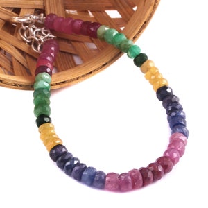 Może przedstawiać: Bransoletka z wielokolorowych kamieni szlachetnych z czerwonymi, zielonymi, żółtymi, niebieskimi i fioletowymi koralikami. Bransoletka wykonana jest z fasetowanych kamieni szlachetnych i ma srebrną klamrę.