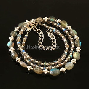 Puede incluir: Un collar de tres hebras hecho con cuentas de plata y piedras preciosas de labradorita de forma ovalada. El collar tiene un cierre de cadena de plata.