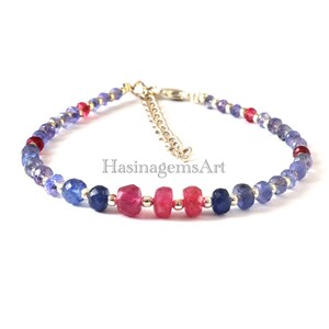 May include: A silver bracelet with blue and pink gemstone beads. The bracelet has a clasp closure and is decorated with a small silver charm that says "HasinagemsArt".