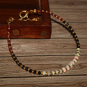 Puede incluir: Un brazalete de oro con cuentas negras, rojas y blancas. El brazalete tiene un cierre de broche.