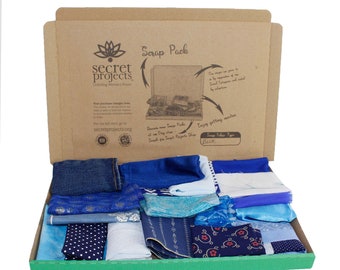 May include: A cardboard box with the text "Scrap Pack" and "Secret Projects" printed on the front. The box is open and filled with a variety of blue fabric scraps.