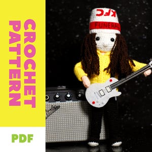 May include: A crocheted doll of a musician wearing a white bucket hat with "KFC FUNERAL" text, a yellow sweater, and black trousers, holding a white guitar. The doll stands in front of a grey amplifier. The image includes the text "CROCHET PATTERN PDF".