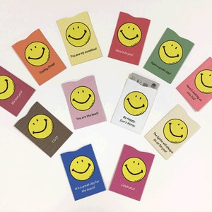 May include: A set of ten colorful card holders with a smiley face design and various positive messages. The messages include "We love you!", "Feeling Great", "TGIF", "You are my sunshine!", "You are the best!", "Here's to you", "Have a great day!", "Be Happy, Don't Worry", "Here's looking at you, kid", and "The lights will always be on for you".