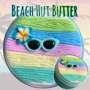 May include: A round container of Beach Hut Butter slime, with layers of green, blue, pink, yellow, and turquoise. The slime is decorated with a blue flower and sunglasses. The text "BEACH HUT BUTTER" is at the top.