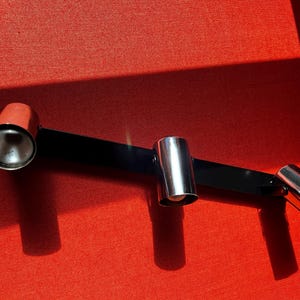 May include: A black track light fixture with three adjustable spotlights. The fixture has a red background.