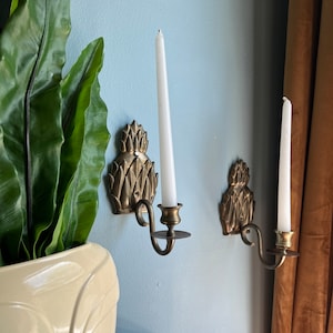 Puede incluir: Dos candelabros de piña dorados con velas blancas en una pared azul claro.