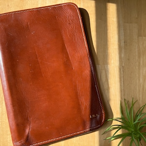 May include: A brown leather portfolio with a zipper closure and the initials "L.H.B." embossed on the front.