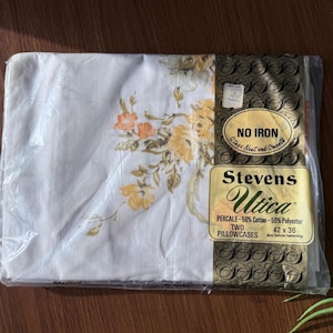 May include: Sealed package of two pillowcases. The pillowcases are white with a floral pattern in shades of orange and yellow. The packaging includes the text "Stevens Utica" and "No Iron". The pillowcases measure 42 x 36 inches.