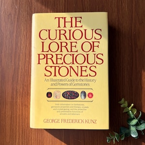 May include: A hardcover book titled "The Curious Lore of Precious Stones" with red text on a yellow background. The book features an illustrated guide to gemstones, their history, and powers. The author's name, George Frederick Kunz, is also visible.