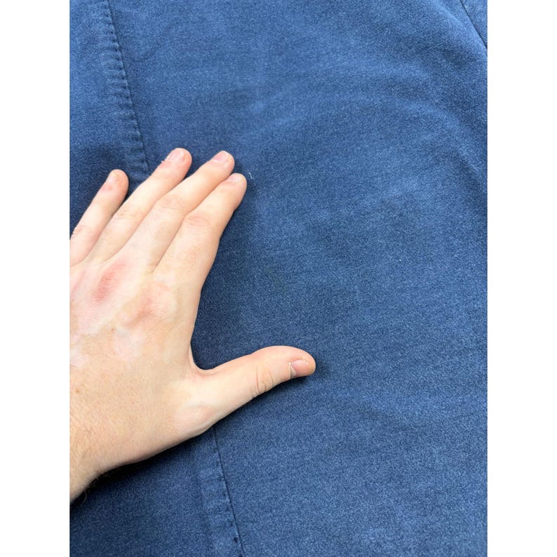 May include: A solid dark blue fabric garment featuring a visible vertical seam running down the left side. The material has a slightly textured, matte finish with a consistent deep navy blue color throughout the visible surface area of the textile.