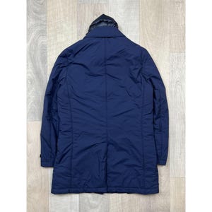 May include: A navy blue, long coat with a black hood. The coat has a button closure and a tailored fit. The back of the coat is visible, showing the seams and the overall shape. The coat is made of a smooth, possibly water-resistant material.