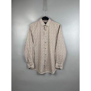 May include: A long-sleeve button-down shirt featuring a repeating vertical pattern of small red, green, and blue floral motifs on a light beige background. The shirt includes a standard collar, a front button placket, and buttoned cuffs.