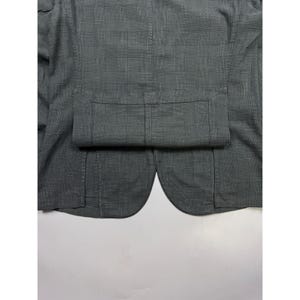 May include: A charcoal gray blazer featuring a subtle glen plaid pattern. The garment displays a structured back panel with a horizontal seam detail across the mid-section and curved hem edges at the bottom, showcasing a woven fabric texture.