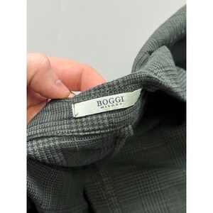 May include: A pair of dark gray trousers featuring a subtle plaid pattern. The garment includes a white interior label with the text Boggi Milano printed in black. The fabric has a textured weave and the trousers are shown from the waist area.