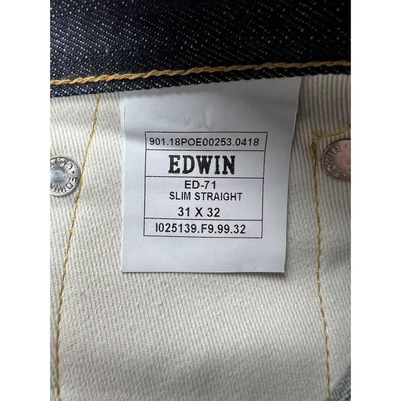 May include: A pair of dark blue denim jeans featuring a white interior tag with the text EDWIN, ED-71, SLIM STRAIGHT, 31 X 32, and additional serial numbers. The jeans include metallic silver rivets embossed with the brand name EDWIN.
