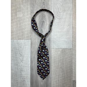 May include: A dark blue necktie featuring a repeating pattern of small, colorful illustrations of birthday cakes, wrapped gifts, and yellow cartoon figures. The tie is tied in a simple knot, displaying a pointed end and a smooth fabric texture.