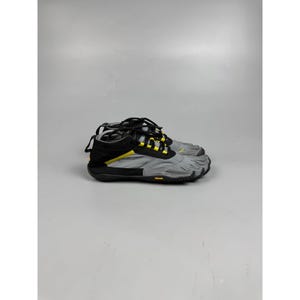May include: A pair of grey and black five-toe shoes featuring individual toe compartments, black laces, and bright yellow accents. The footwear includes a black Vibram rubber sole and a low-top design with a textured grey fabric upper section.