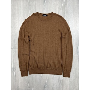 Puede incluir: Un suéter marrón de cuello redondo con detalles acanalados. El suéter de manga larga tiene un corte clásico y una pequeña etiqueta en el cuello. La prenda está hecha de un material suave y se muestra sobre una superficie clara con vetas de madera.