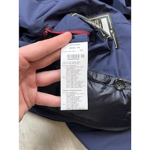 May include: Navy blue jacket with a black lining and a tag with product information. The tag includes the size 46 and the fabric composition: 54% Polyamide, 46% Polyurethane. The jacket has a button closure.