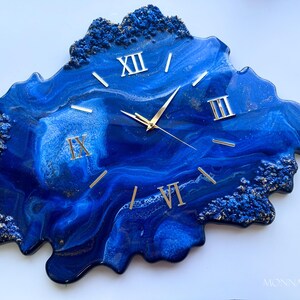 May include: Blue and gold resin clock with Roman numeral markings. The clock face is an abstract design with blue and gold swirls.