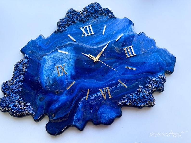 May include: Blue and gold resin clock with Roman numeral markings. The clock face is an abstract design with blue and gold swirls.