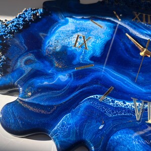 May include: A blue and white resin clock with gold Roman numeral hour markers and gold hands. The clock face has a unique, abstract design that resembles swirling water.