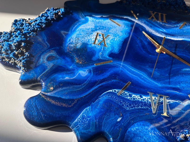 May include: A blue and white resin clock with gold Roman numeral hour markers and gold hands. The clock face has a unique, abstract design that resembles swirling water.