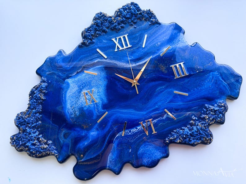 May include: Blue and gold resin wall clock with Roman numeral markings. The clock face is an abstract design with a blue and white marbled effect.
