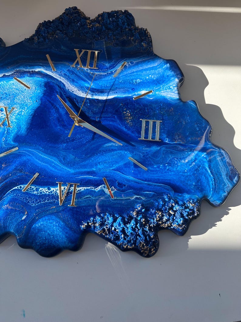 May include: Blue resin clock with gold Roman numeral markings and a white background. The clock face is shaped like a wave.