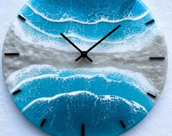 Puede incluir: Un reloj redondo con un diseño de olas de mar azules y blancas. La esfera del reloj está hecha de resina y tiene agujas y marcadores de hora negros.