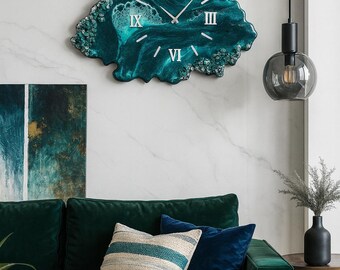 May include: A teal resin wall clock with silver numerals, shaped like a cloud. The clock is mounted on a white marble wall. The room also features a green velvet sofa with decorative pillows and a black pendant light.