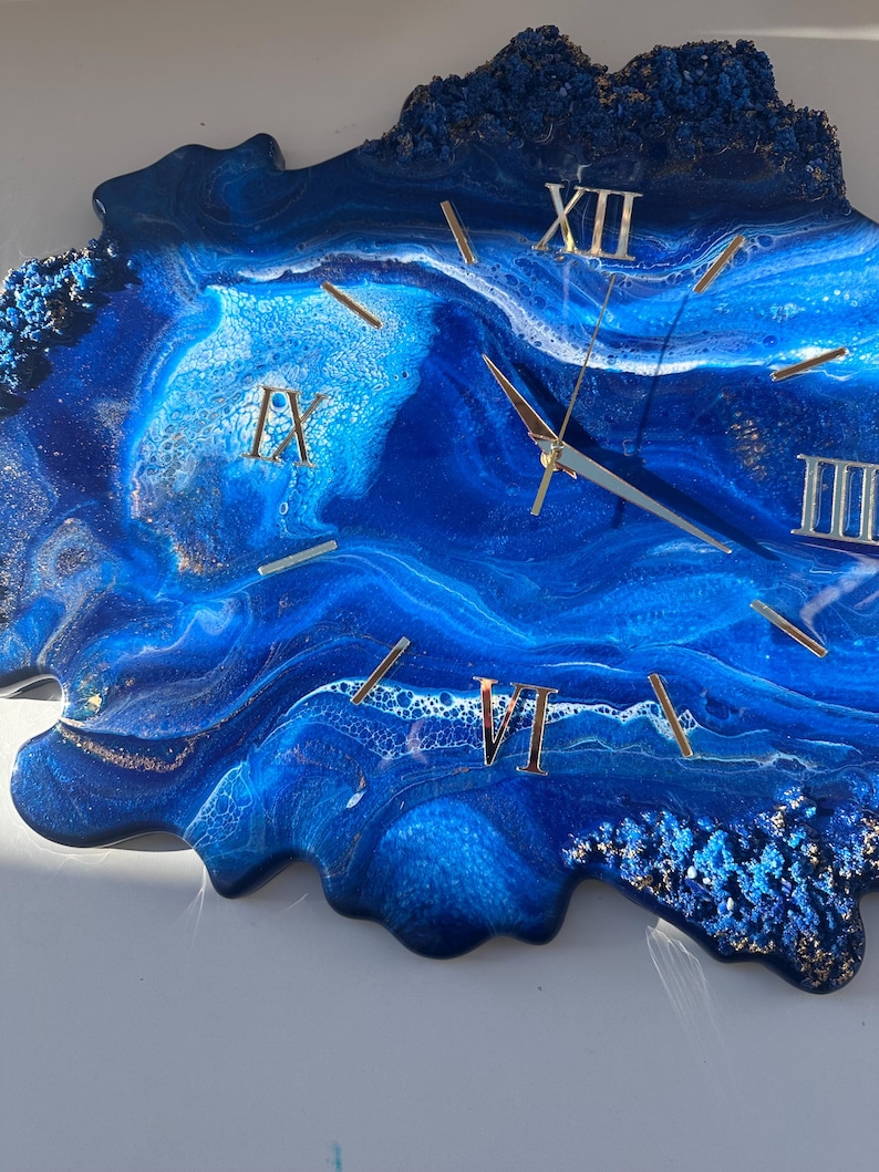 May include: Blue and white resin clock with gold Roman numeral markings. The clock face is a unique abstract design with a blue and white swirl pattern.