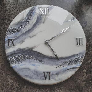 May include: A white and gray clock with silver Roman numeral markings and silver hands. The clock face has a marbled design with silver glitter embedded in the resin.