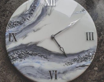 May include: A white and gray clock with silver Roman numeral markings and silver hands. The clock face has a marbled design with silver glitter embedded in the resin.