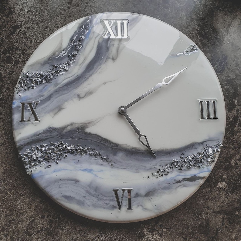 May include: A white and gray clock with silver Roman numeral markings and silver hands. The clock face has a marbled design with silver glitter embedded in the resin.