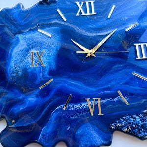 May include: Blue and gold resin clock with Roman numeral markings. The clock face is a swirling blue and white abstract design with gold accents.